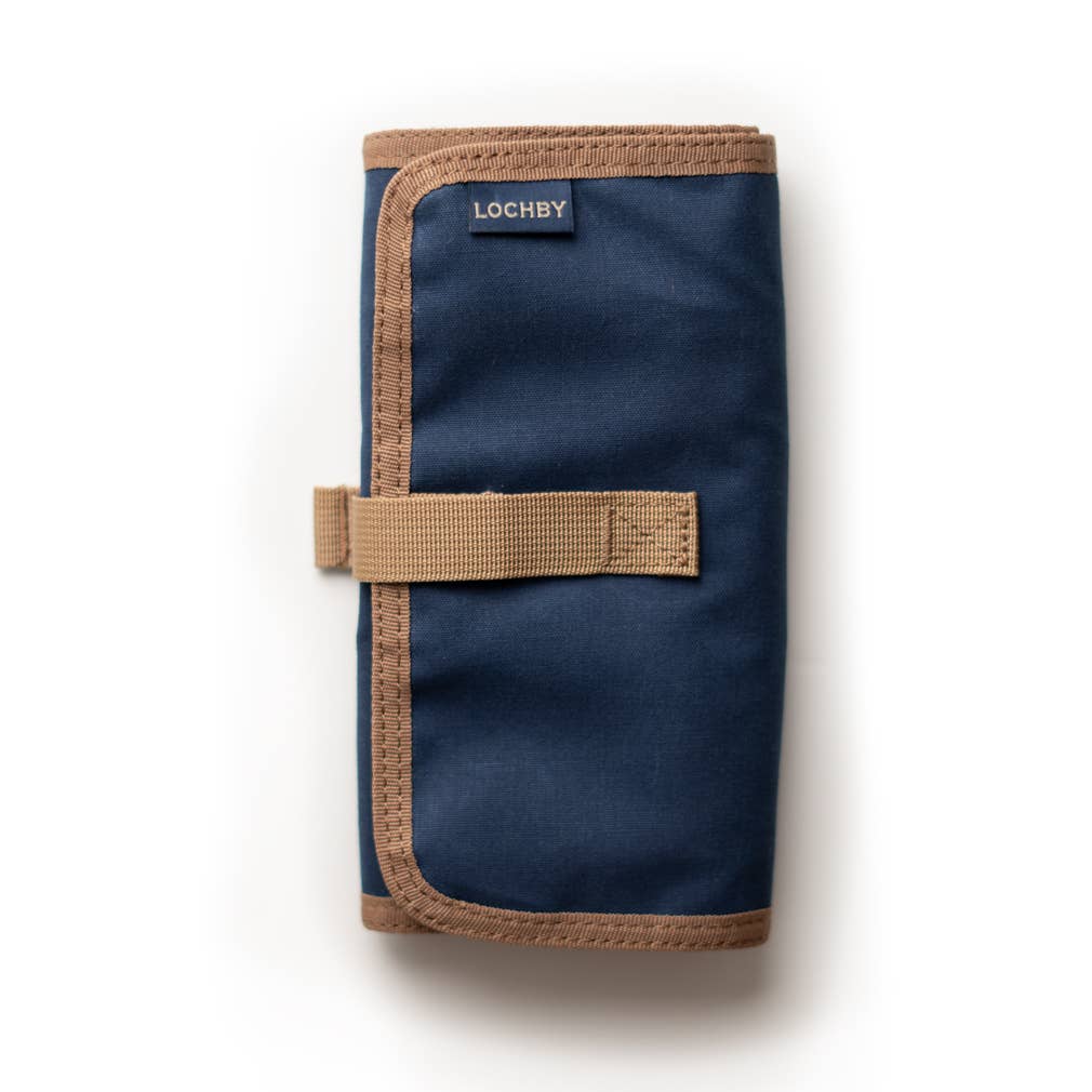 A partially unrolled tool roll with a brown waxed canvas exterior, aluminum hook fastener, and multiple pockets containing pens and other tools.