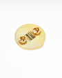 A round textured gold pin-back badge or lapel pin with two small gold oval studs and a central gold rectangular detail, photographed on a clean white background.