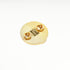 A round textured gold pin-back badge or lapel pin with two small gold oval studs and a central gold rectangular detail, photographed on a clean white background.