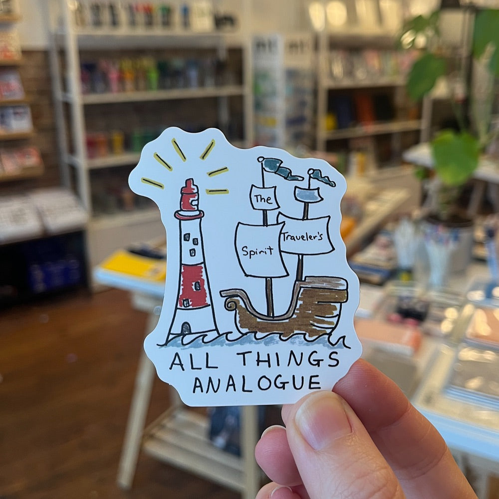 Sticker with a lighthouse and ship design held in front of a store shelf.