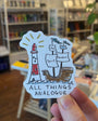 Sticker with a lighthouse and ship design held in front of a store shelf.