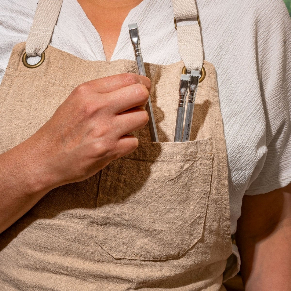 Person wearing a beige apron with tools in a pocket, holding a tool.