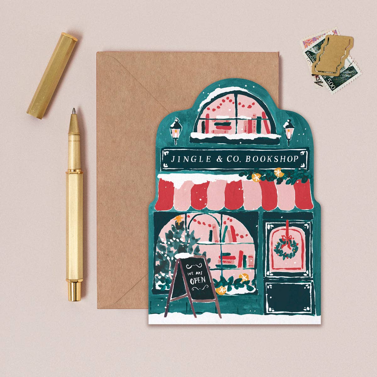 Greeting card with a festive bookshop illustration, envelope, pen, and stickers on a beige background