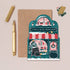 Greeting card with a festive bookshop illustration, envelope, pen, and stickers on a beige background