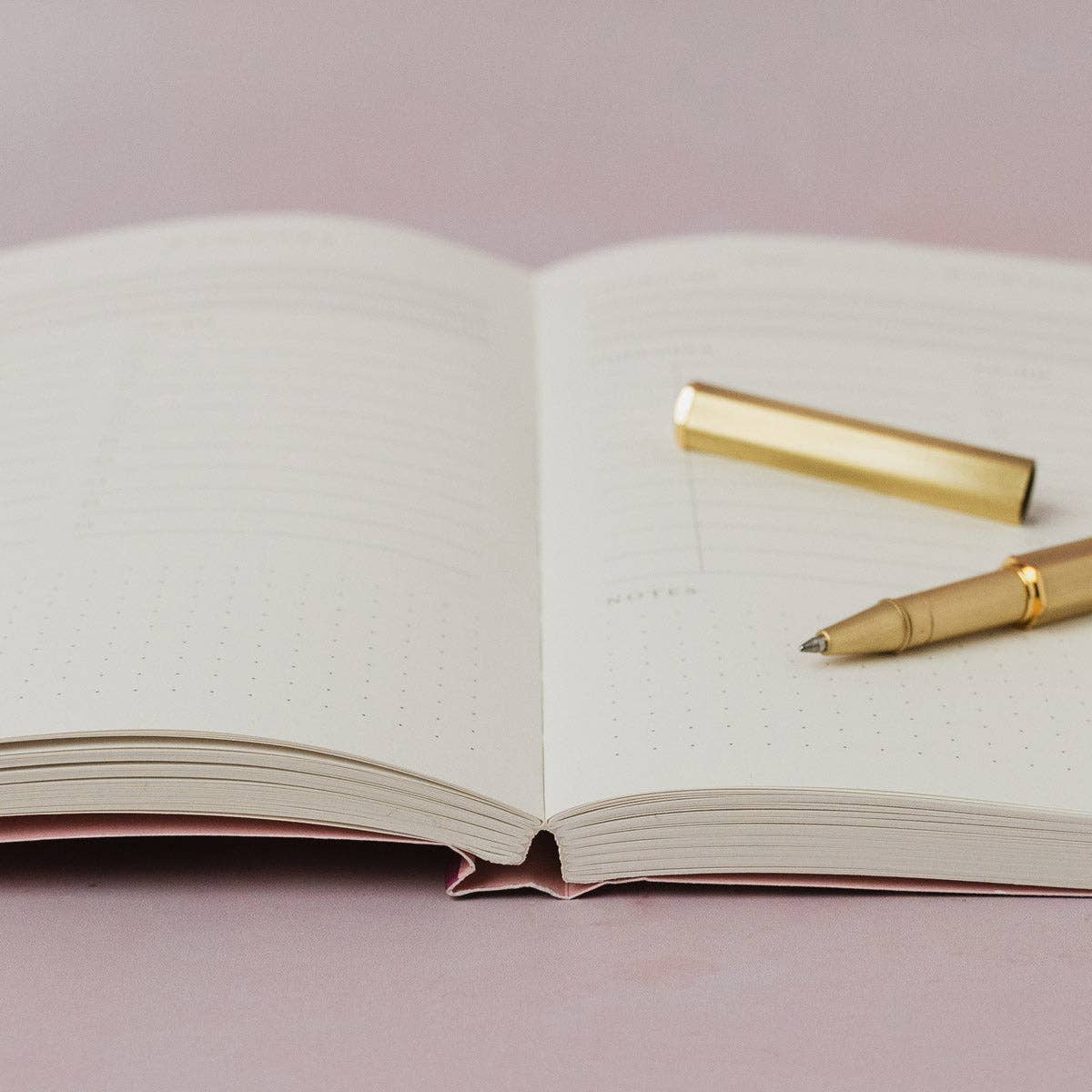 Open notebook with a gold pen on a light pink background