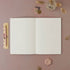 Open notebook on a pink surface with decorative items around