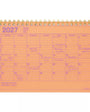 An orange 2027 spiral-bound desk calendar with pink printed grid lines and handwritten notes in purple ink, shown on a white background.
