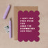 A square greeting card with a scalloped magenta border and white text reading, 'I LOVE YOU, EVEN WHEN YOU LOAD THE DISHWASHER LIKE THAT.' It is shown on a kraft paper background with a matching envelope, a lavender pen, and a small postage stamp.