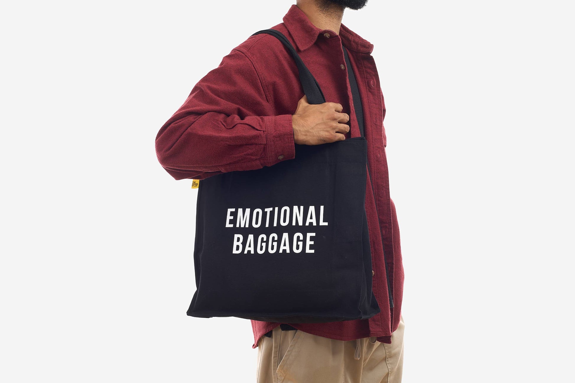Person holding a black tote bag with 'EMOTIONAL BAGGAGE' text on a white background