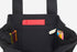 Black tote bag with colorful pens and a red pocket on a white background