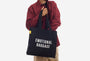 Person holding a black tote bag with 'EMOTIONAL BAGGAGE' text on a white background