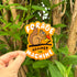 Sticker with a squirrel design and text 'Forage Against the Machine' held in front of green foliage.