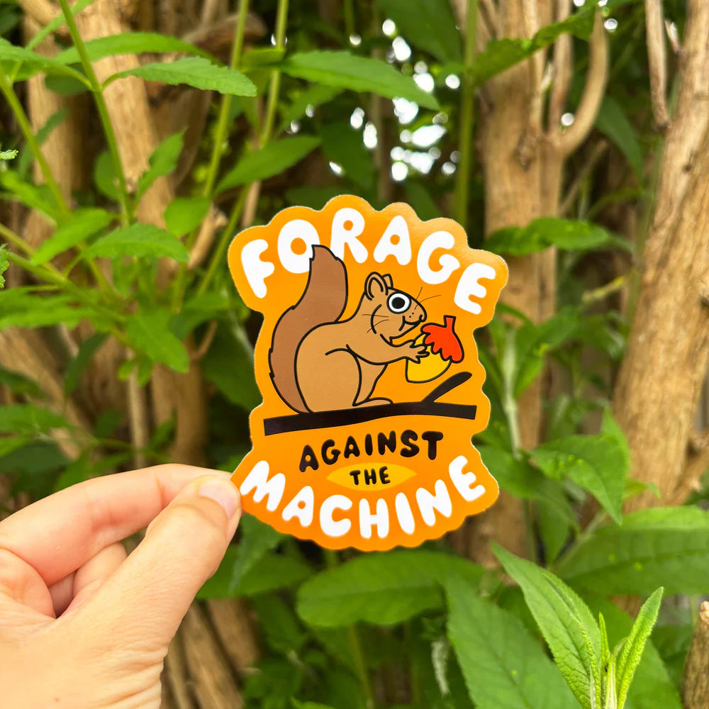 Sticker with a squirrel design and text 'Forage Against the Machine' held in front of green foliage.