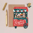 A Christmas-themed greeting card from 'The Gingerbread Bakery' styled in a flat-lay arrangement on a light beige background, accompanied by a brown envelope, a gold pen, and a gold cap.