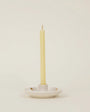 White ceramic candle holder with a single beige candle on a light beige background
