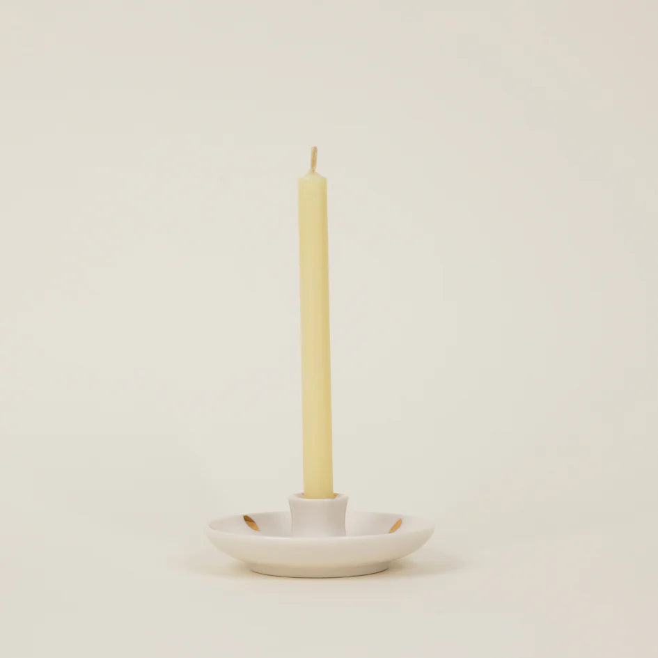 White ceramic candle holder with a single beige candle on a light beige background