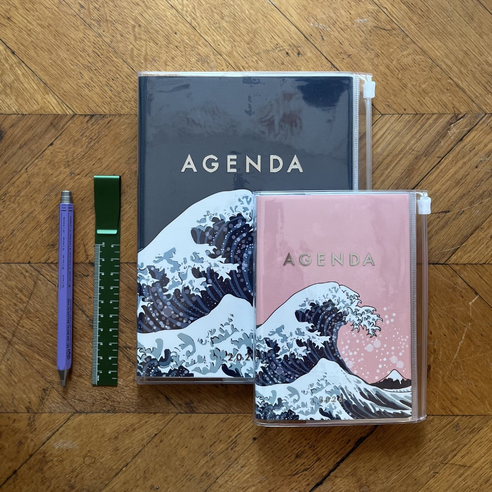 Two agendas with wave design on a wooden surface with a pen and ruler.
