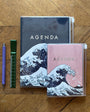 Two agendas with wave design on a wooden surface with a pen and ruler.