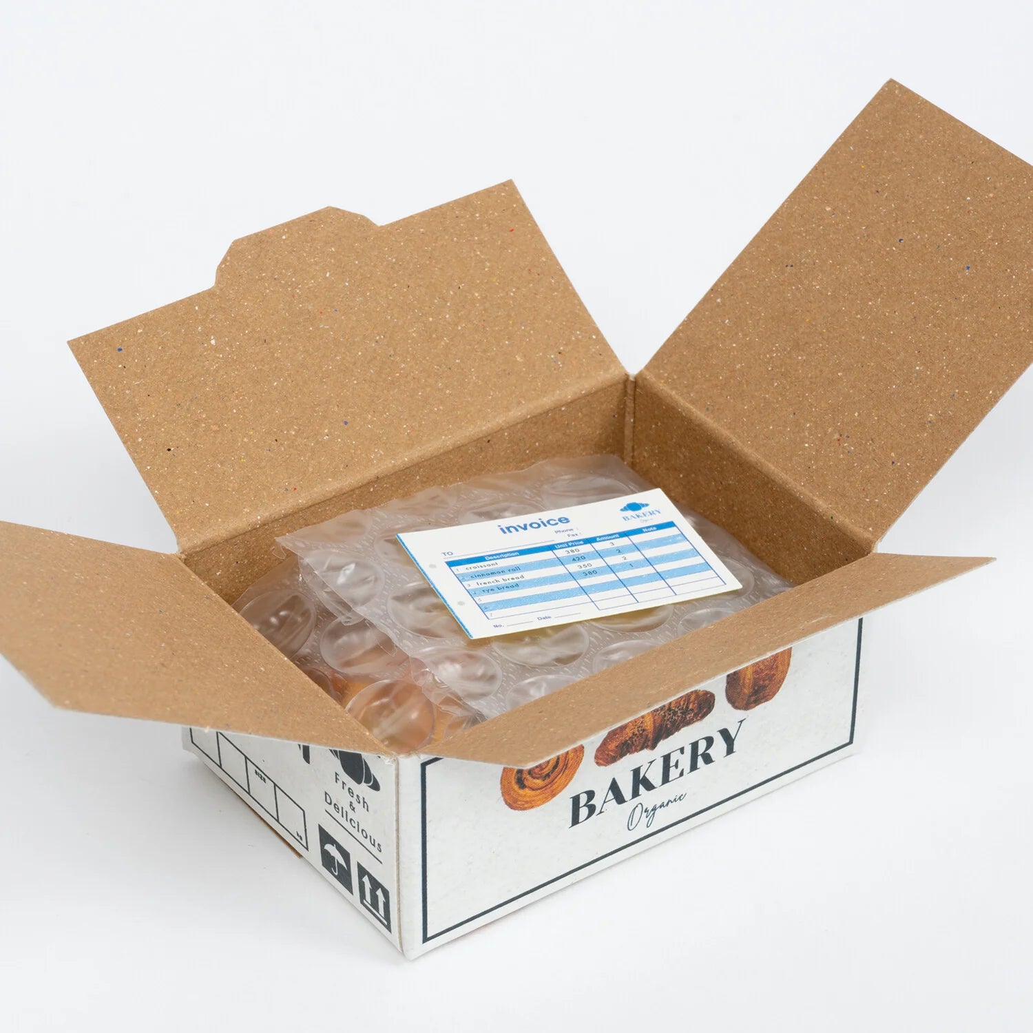 Open cardboard box with bakery branding, containing ice packs and an invoice on a white background