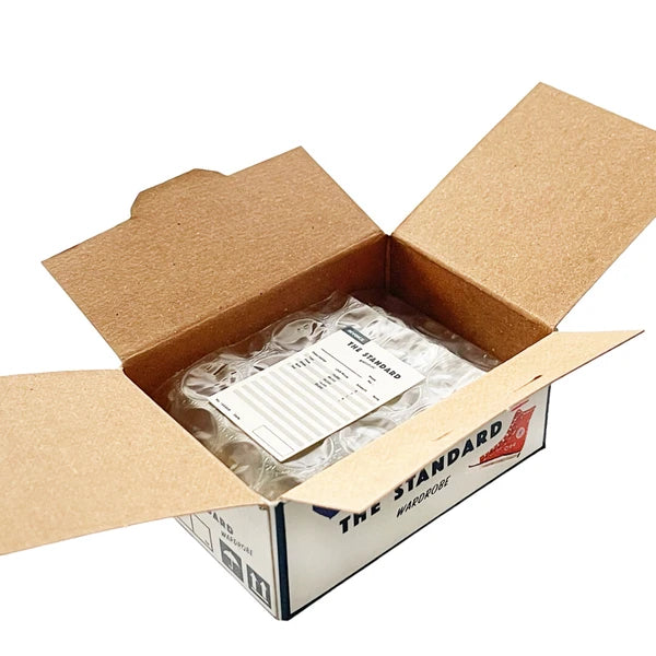 Open cardboard box containing a clear plastic bag with white labels, branded 'The Standard'.