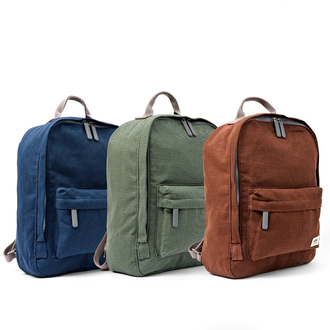Three canvas backpacks in navy blue, sage green, and rust brown, arranged side-by-side on a clean white background.