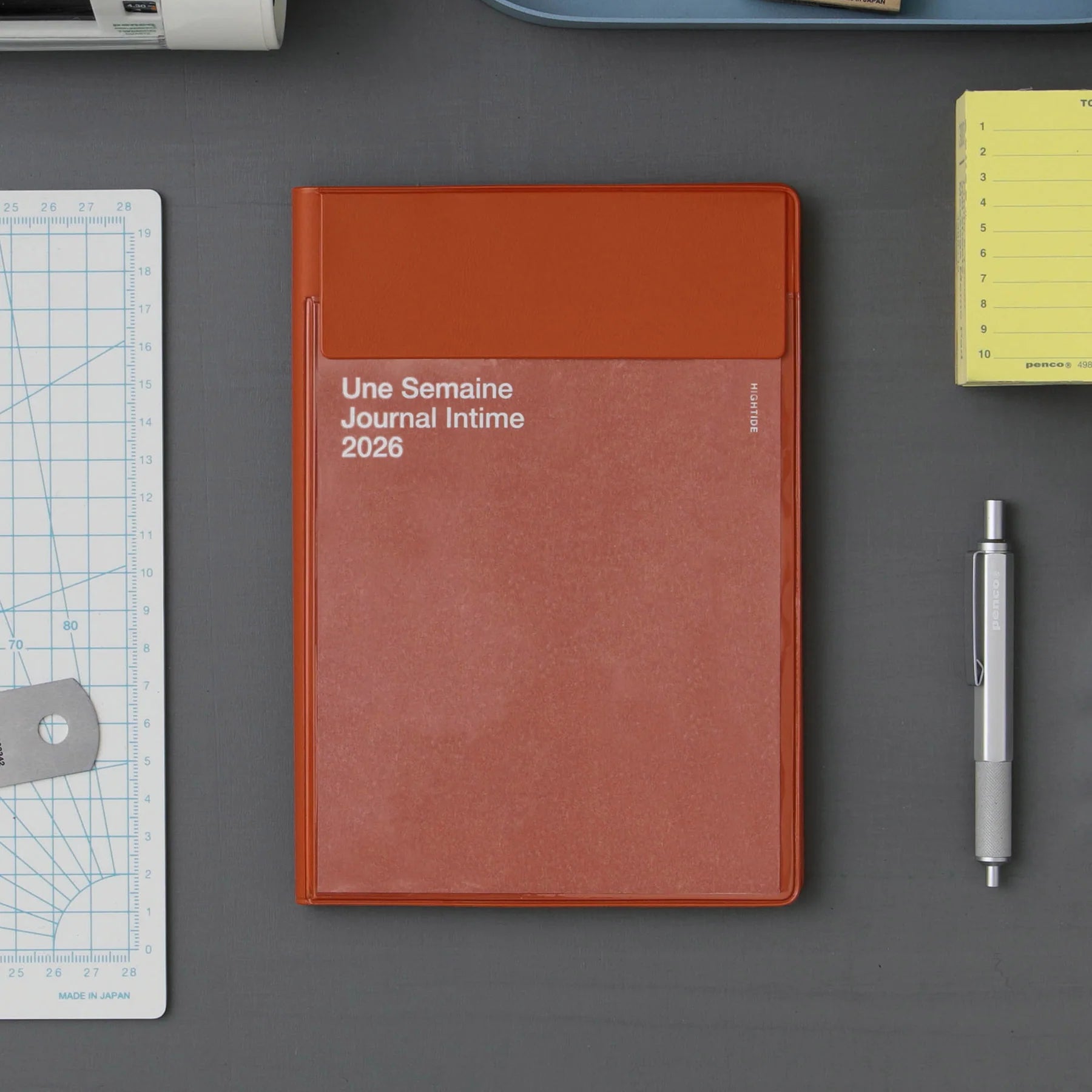 Fox Red notebook titled 'Une Semaine Journal Intime 2026' on a gray surface with a pen and ruler.