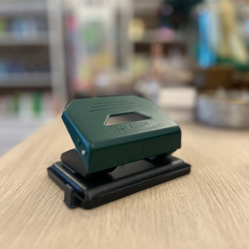 Green and black hole puncher on a wooden surface with a blurred background