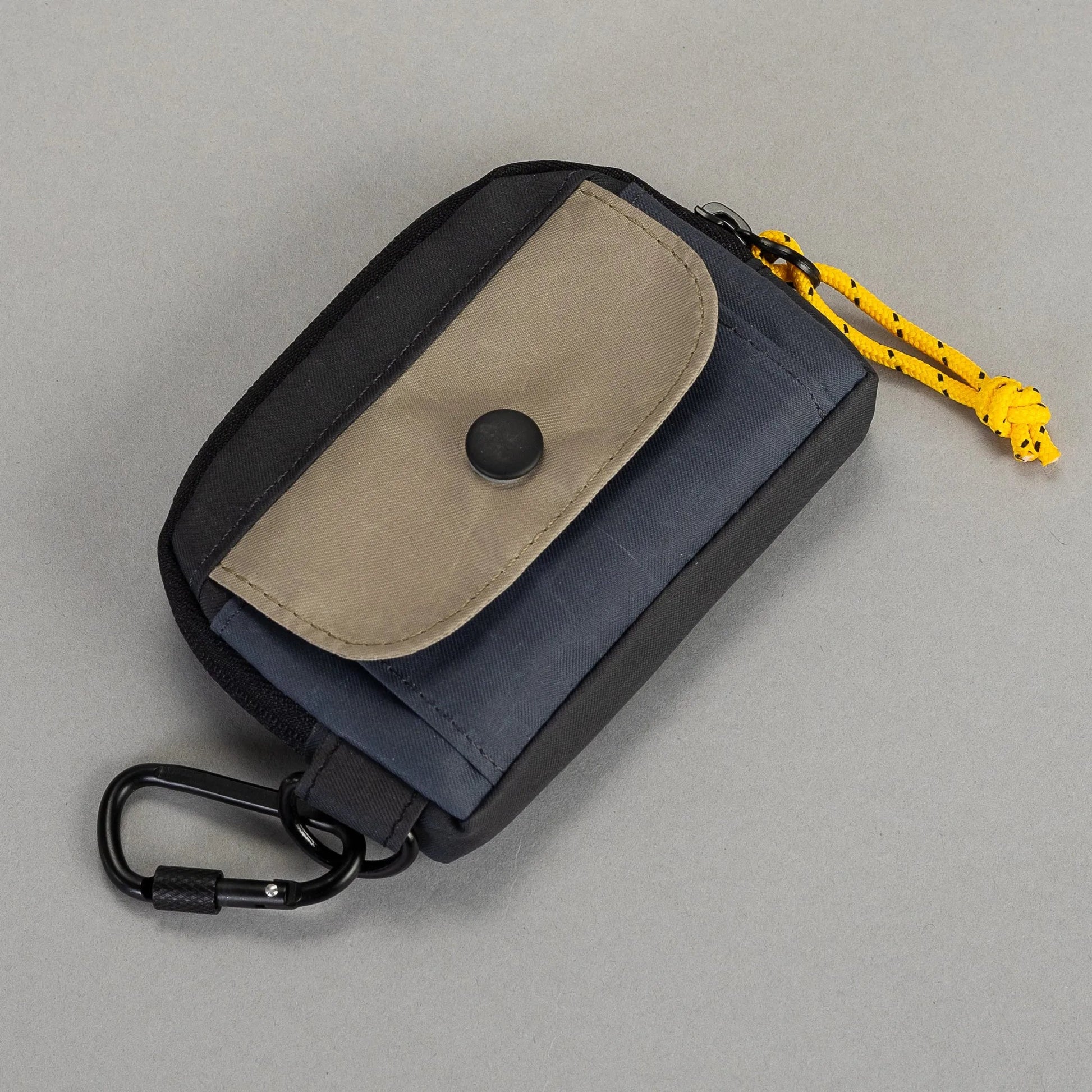 Small pouch with beige flap and black carabiner on a gray background