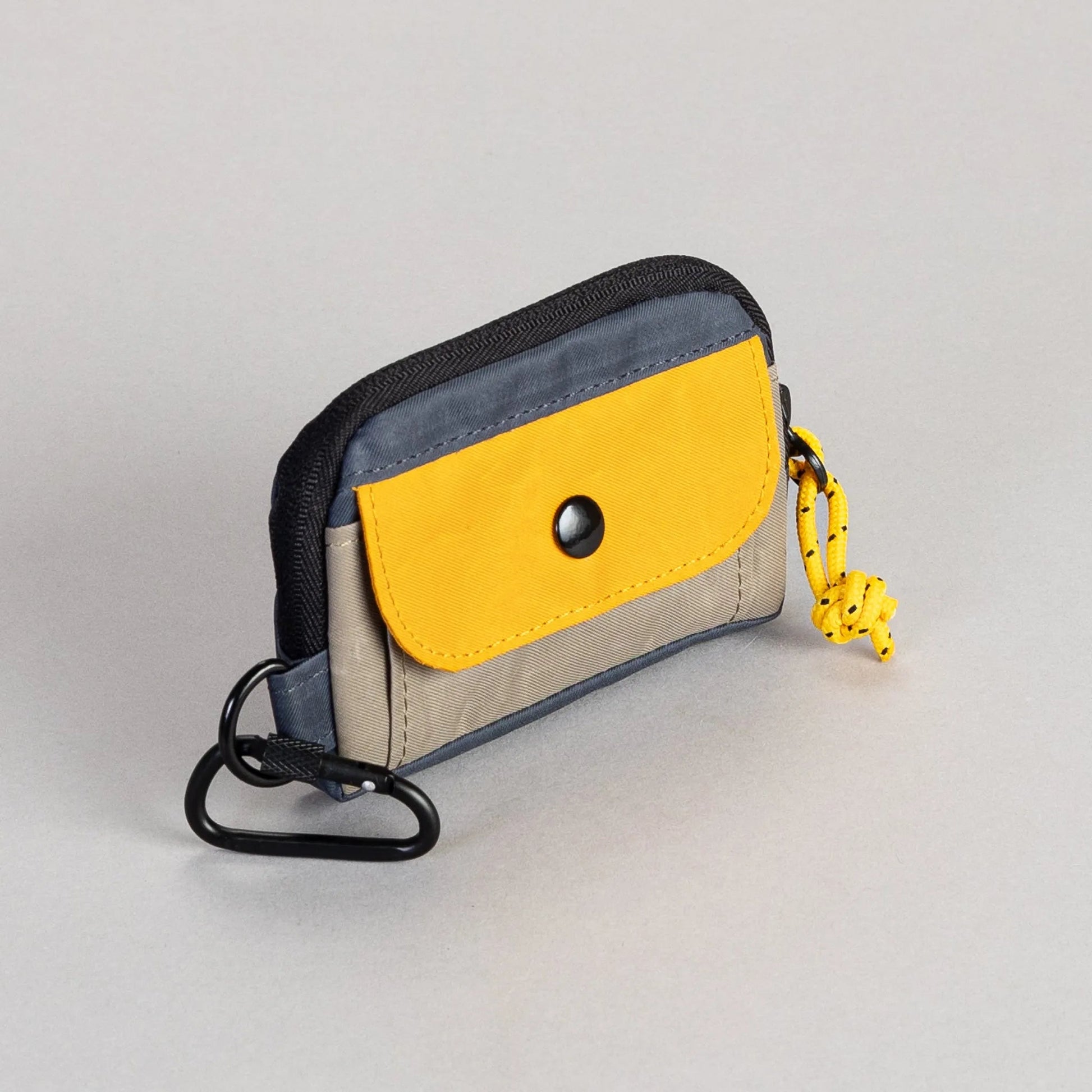 Small pouch with yellow flap and black strap on a light gray background