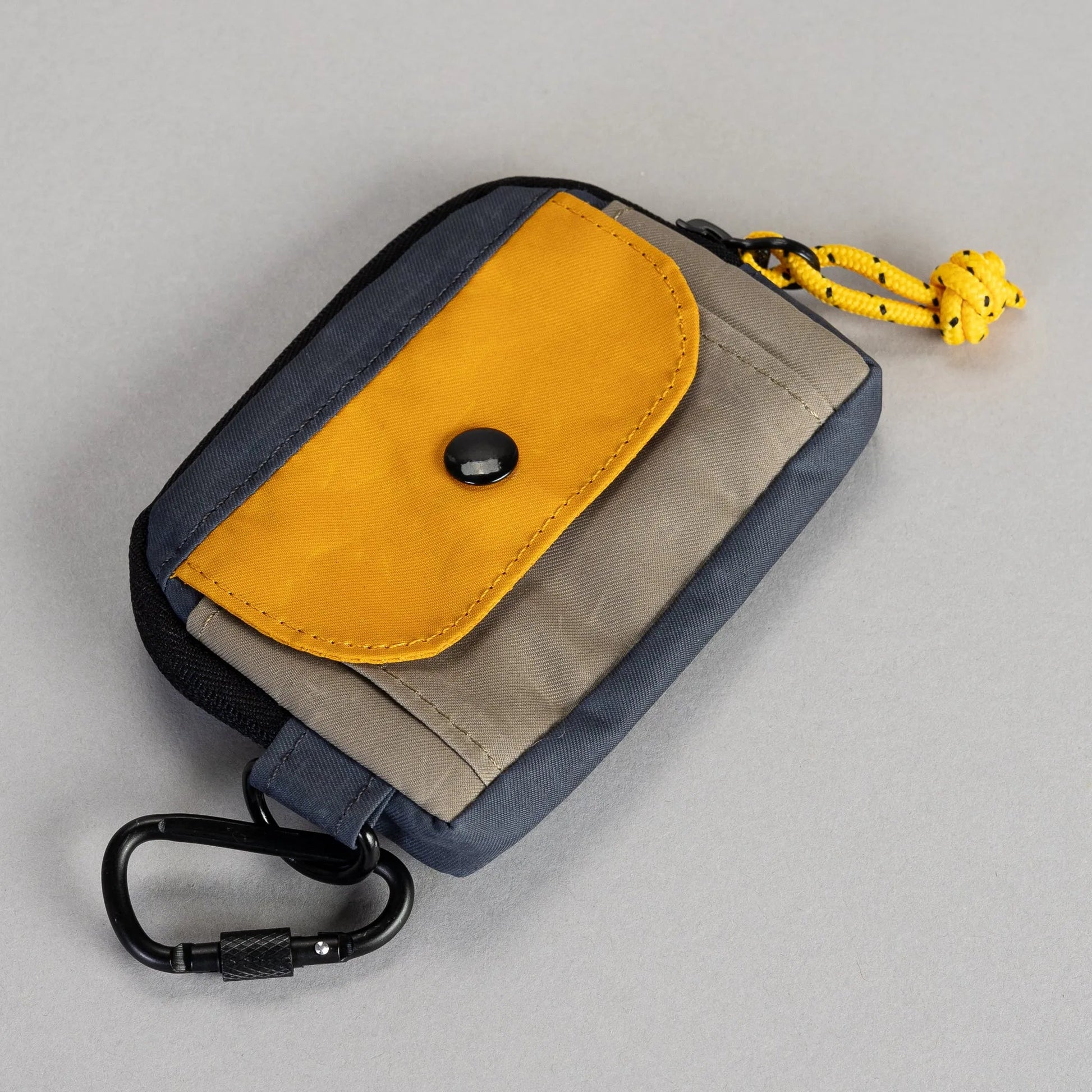 Small pouch with yellow flap and carabiner on a gray background