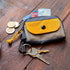 Small wallet with yellow flap, coins, keys, and cards on a wooden surface