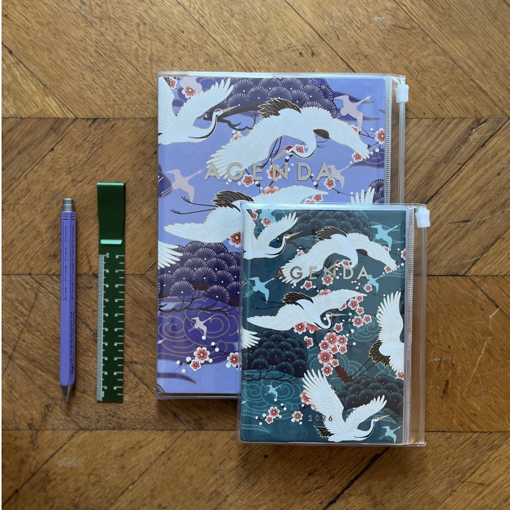 Two notebooks with crane designs on a wooden surface with a pen and ruler.
