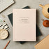 Pink notebook with branding on a gray surface with stationery items