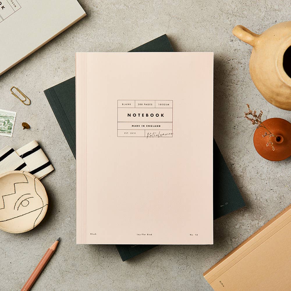 Pink notebook with branding on a gray surface with stationery items