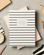 Striped notebook on a textured surface with stationery items