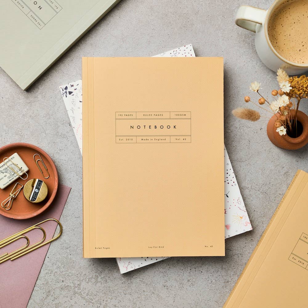 Beige notebook on a gray surface with office supplies and a cup of coffee.