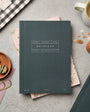 Hunter Green notebook on a gray surface with stationery items around