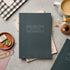 Hunter Green notebook on a gray surface with stationery items around