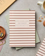 Striped notebook on a gray surface with office supplies and a cup of coffee.