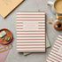 Striped notebook on a gray surface with office supplies and a cup of coffee.