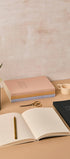 Open notebook with a pen, closed books, and decorative items on a beige surface.