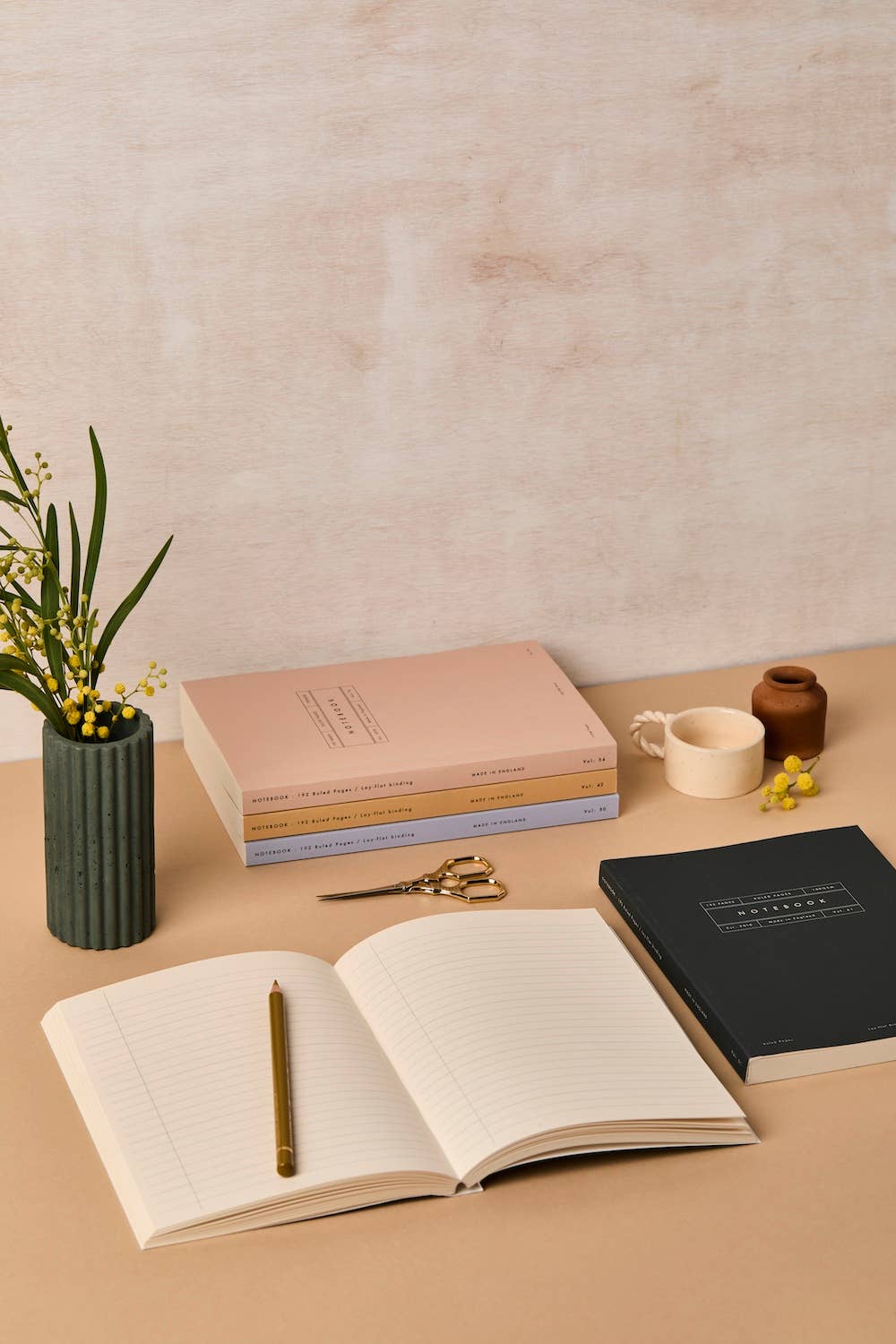 Open notebook with a pen, closed books, and decorative items on a beige surface.
