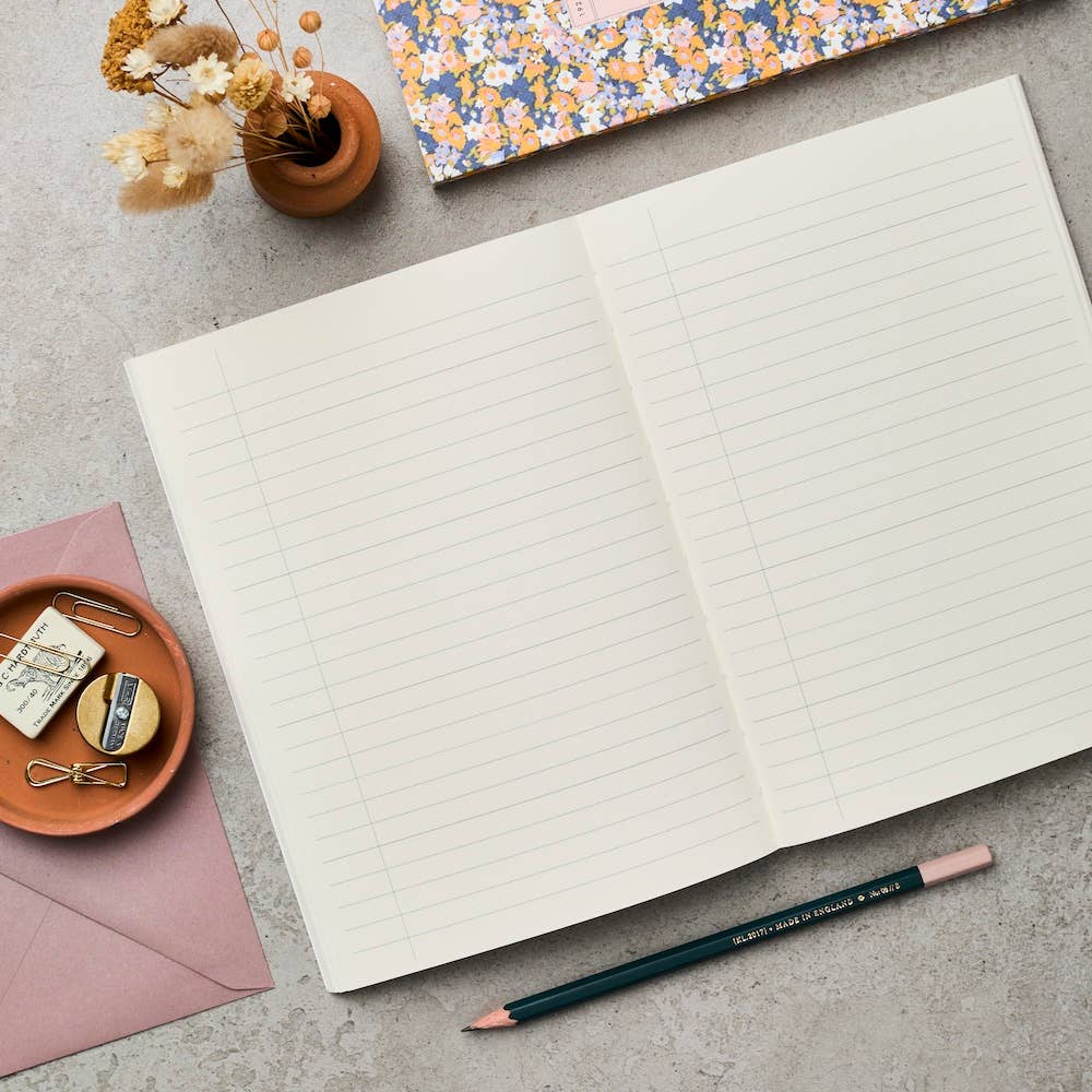 Open notebook with lined pages on a gray surface, surrounded by stationery items.
