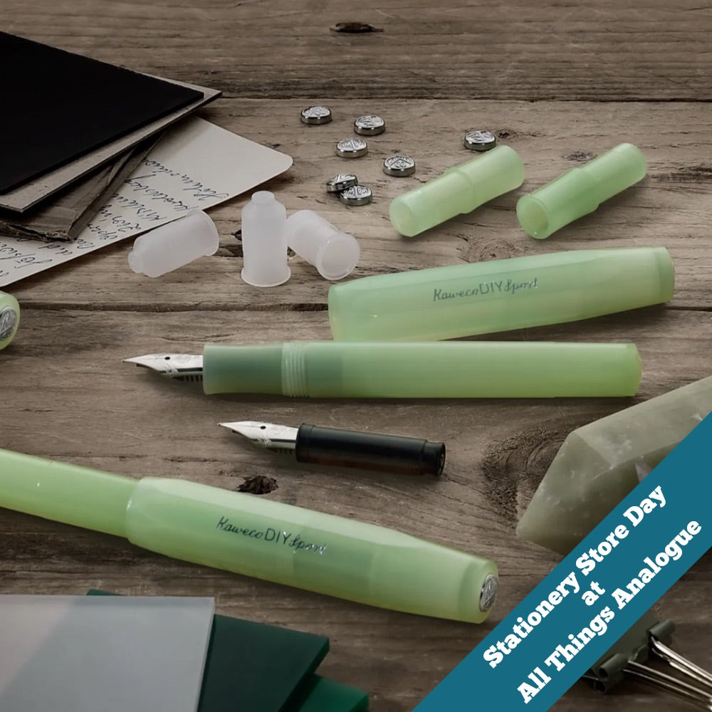 Green fountain pens and ink cartridges on a wooden surface with stationery items.