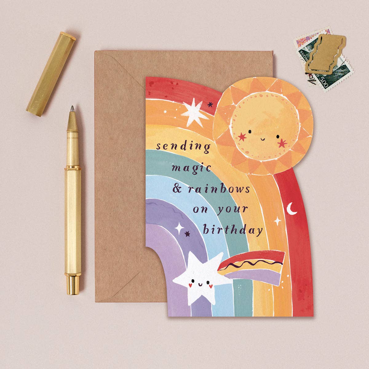 Colorful birthday card with sun and rainbow design, pen, and envelope on beige background