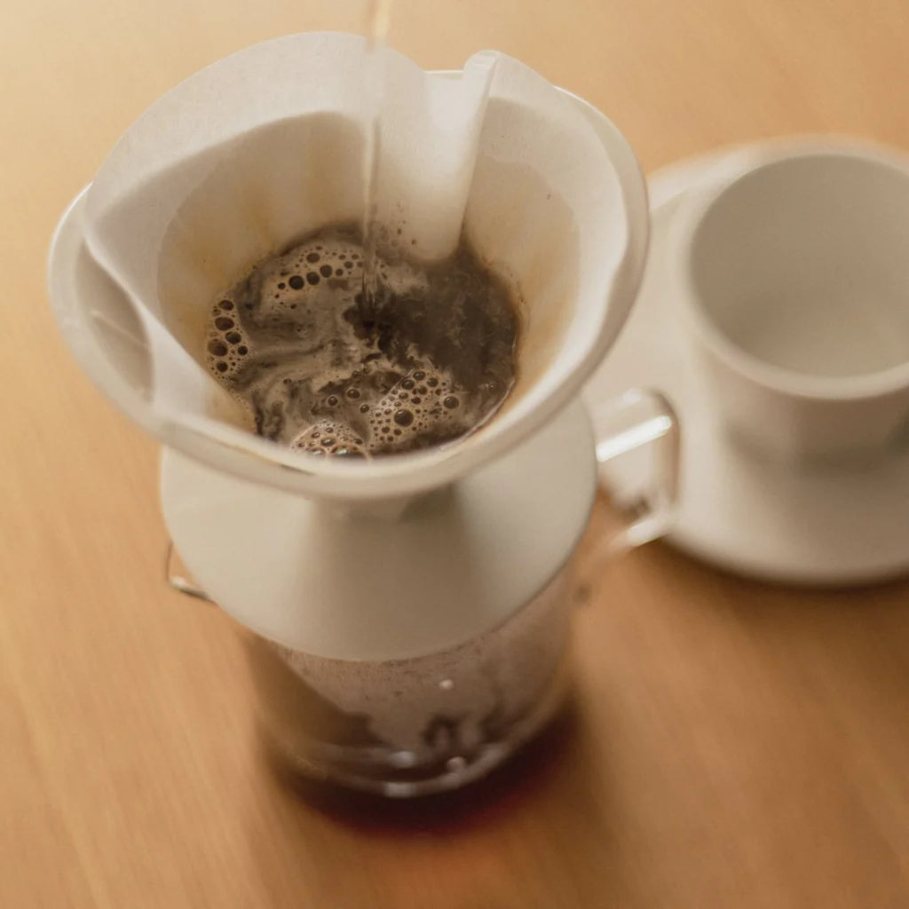 Coffee being brewed in a white pour-over coffee maker on a wooden surface.