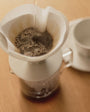Coffee being brewed in a white pour-over coffee maker on a wooden surface.