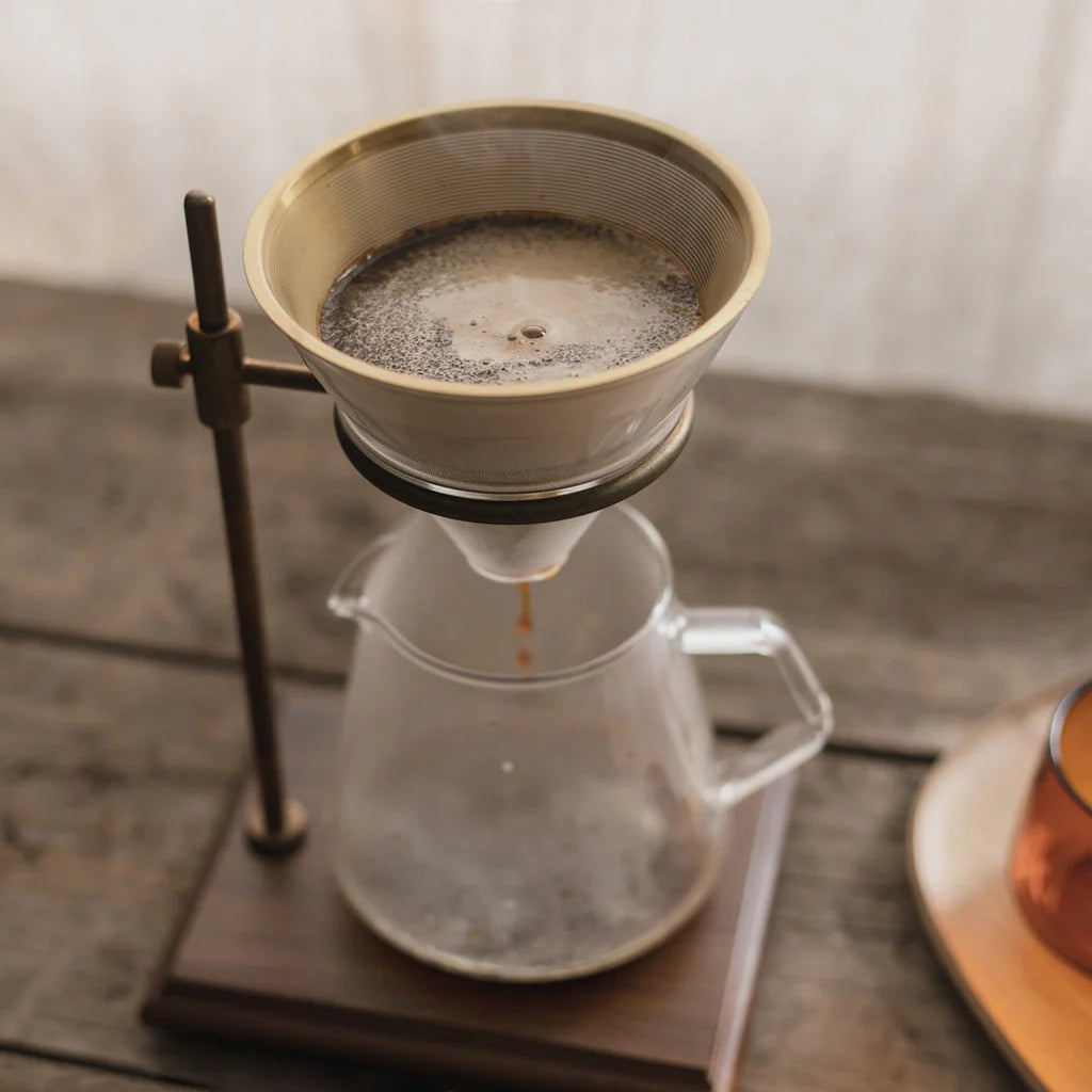 Coffee brewing process using a pour-over setup with a glass carafe and metal stand.