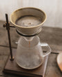 Coffee brewing process using a pour-over setup with a glass carafe and metal stand.
