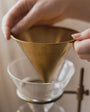 Person holding a gold coffee filter over a glass container